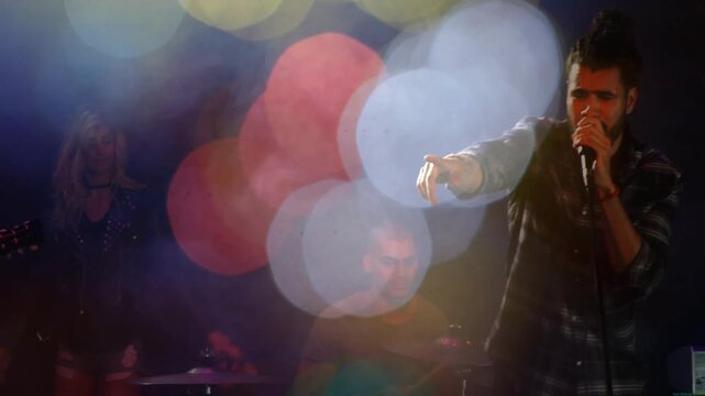 Lead vocalist moving from pointing to clasping mic as song building, bokeh shifting, revealing band