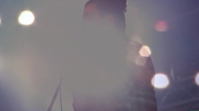 Male singer singing cupping vintage mic while stage lights causing flares and shadow for music gig