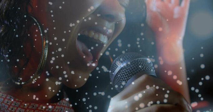 Female singer bringing mic near and building vocal power in music, snowy particles across frame