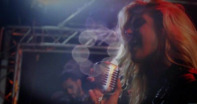 Female singer starting set, holding mic on music stage, lights causing bokeh and guitarist playing