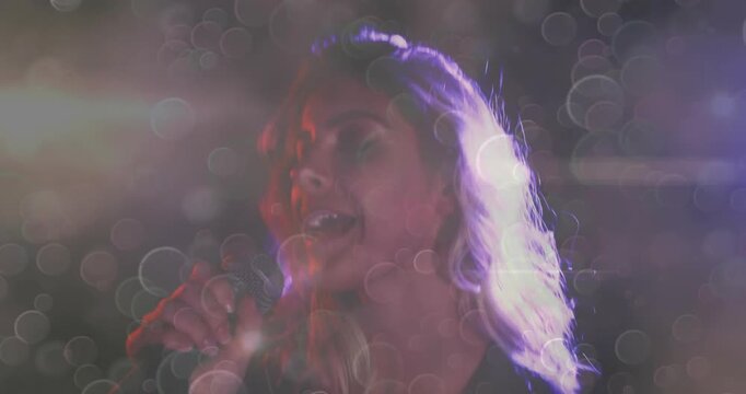 Camera moving closer and female singer adjusting microphone, singing for music fans amid lens bokeh