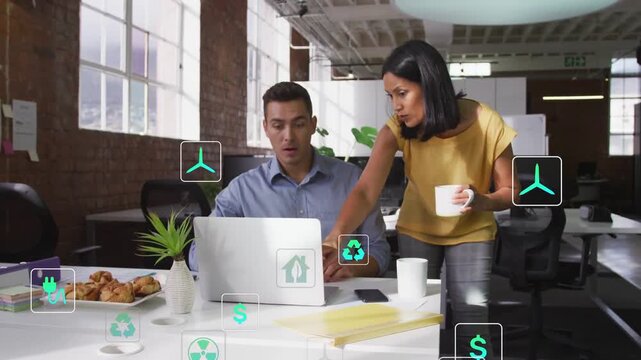 Manager pointing and tapping laptop, initiating green finance icons multiplying, colleague learning
