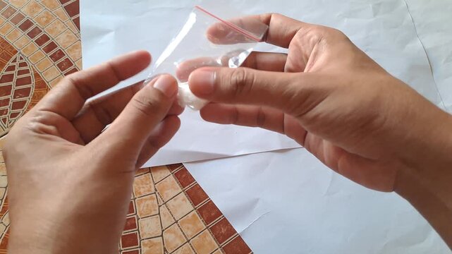 Close-up of Asian male hands demonstrating the dangers of illegal drugs using capsules and a small plastic bag of white powder as visual aids for drug abuse prevention education.