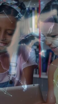 Vertical video: Two girls tapping tablet, causing network lines forming rotating globe for learning