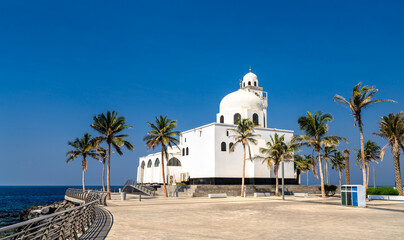The white Island Mosque stands prominently along the Red Sea coast on the Jeddah Corniche in Saudi Arabia, framed by tropical palm trees under a clear blue sky. © Leonid Andronov