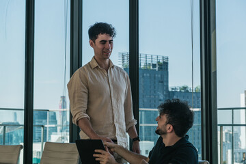 Fototapeta premium Two business colleagues having an informal conversation, collaborating on a project in a modern office with city views