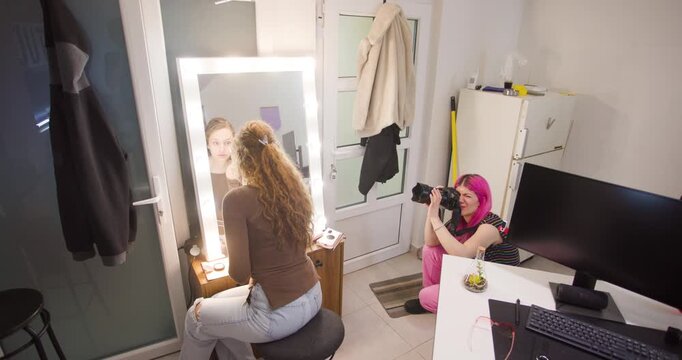 Female Photographer with Pink Hair Captures a Model Preparing for a Photoshoot in a Studio Setting