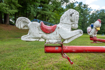 Old metal rocking horse, animal form, riding playground equipment for young children at a park, school, with chipped white and red paint. 