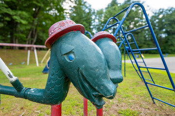 Close up of old metal climbing playground equipment with strange green dinosaur heads and red hats for young children at a park, school. 