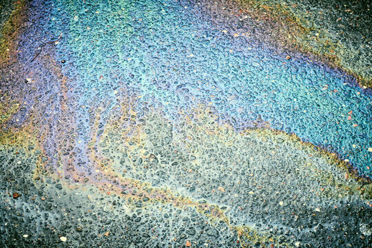 Oil, gasoline, and water mixing on a wet asphalt road surface, forming a vibrant iridescent rainbow slick pattern