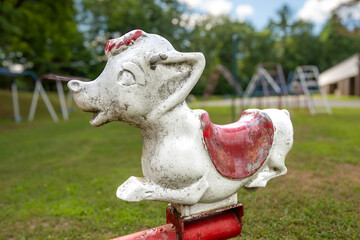 Old metal rocking cow, animal form, riding playground equipment for young children at a park, school, with chipped white and red paint. 