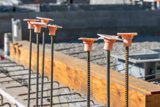 Construction site, with orange rebar caps on steel rebar stub ups in a reinforced concrete wall, foundation to protect construction workers and building materials.
