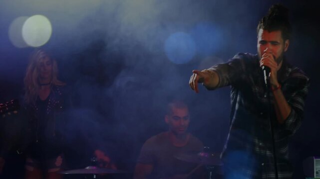 Lead singer stepping forward on music cue, pointing toward crowd and singing amid blue-purple bokeh
