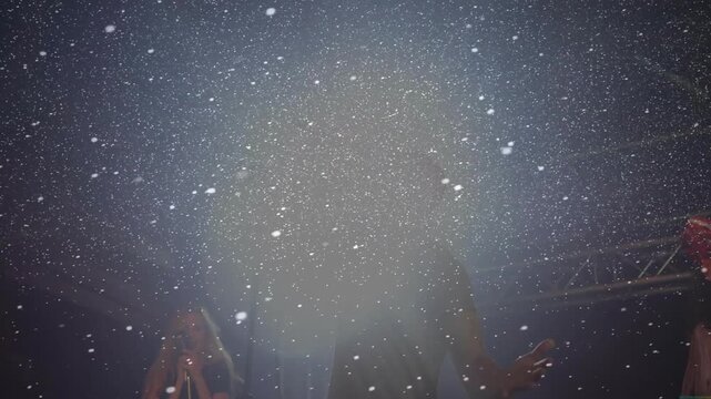 Male lead singer singing, raising mic for concert climax, sparking snow burst creating backlit halo