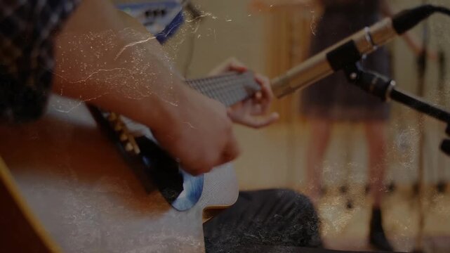 Seated guitarist strumming switching to plucking as mic moving in, capturing studio grain overlay