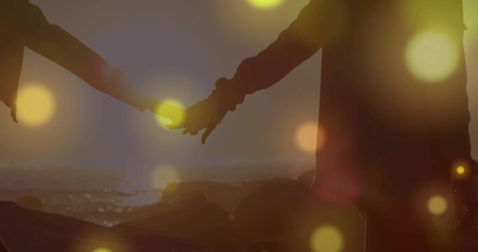 Couple reaching, fingertips meeting then walking rocky coast at sunset, film bokeh overlaying forms