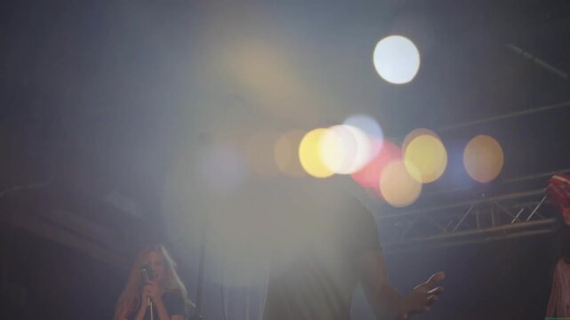 Male lead singer raising mic singing duo shaking tambourine amid lens flare energizing music crowd