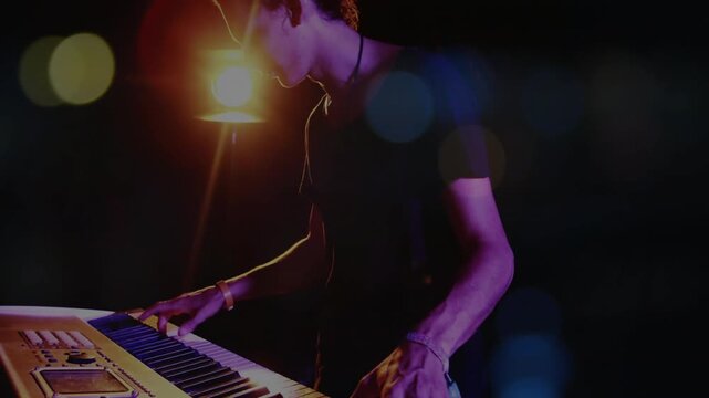 Musician pressing keys and shifting hands while creating ambient synth music with warm lamp bokeh