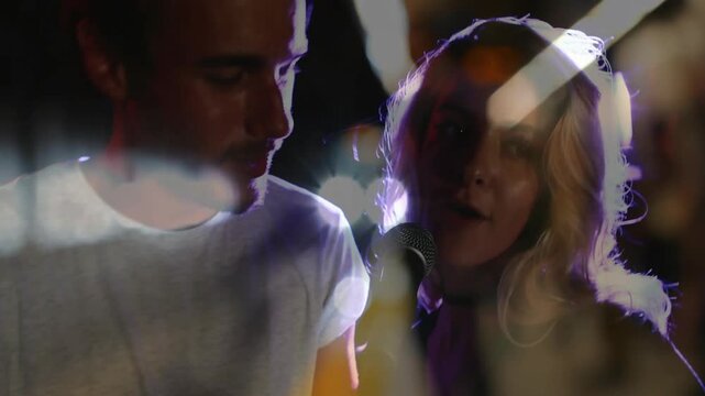 Female leaning into mic and male joining, singing duet in music studio, bokeh flares blending faces