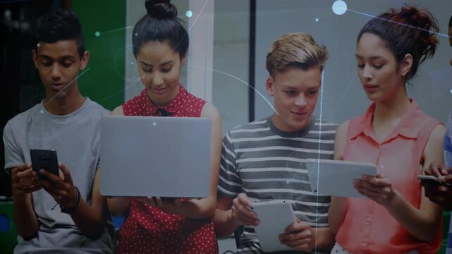 Rightmost lifting tablet starting classmates leaning in and sharing screens to compare content