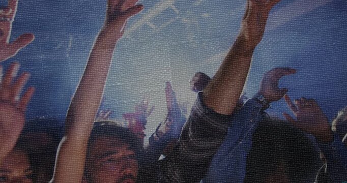 Concert crowd raising arms, forming silhouettes while stage light flaring triggers cheering