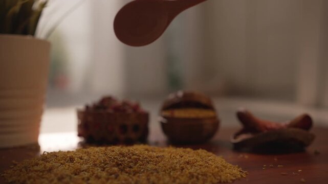 Slow zoom in close up of a hand using a wooden spoon to scoop and pour dried Osmanthus flowers on wood, in warm natural morning light, herbal tea concept.