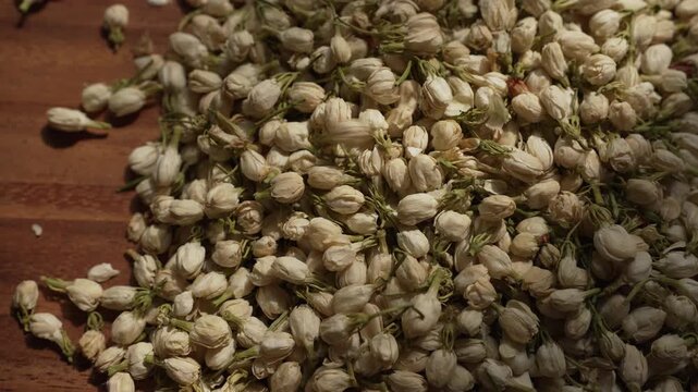 Cinematic top view slow zoom in transitioning to a sharp focus on dried jasmine buds falling onto rustic wooden floor, showcasing delicate textures and patterns.