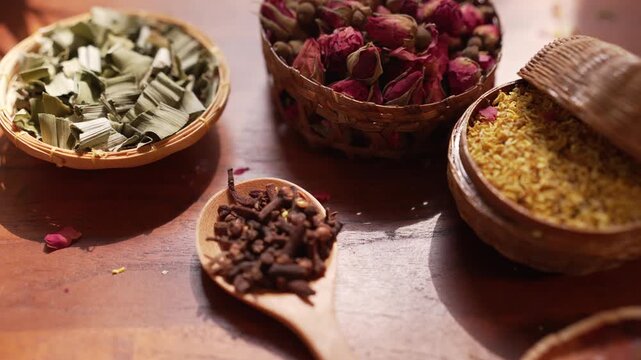 Aesthetic cinematic slow zoom in to detailed dried cloves in a wooden spoon, featuring curated rose buds, jasmine, osmanthus and bael fruit slices on a rustic table by a window with moving sunlight an