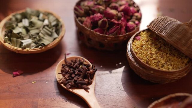Cinematic shift focus on dried rose buds, jasmine, and bael fruit on a wooden table, featuring beautiful moving leaf shadows and sunlight from a breeze for a peaceful wellness atmosphere.