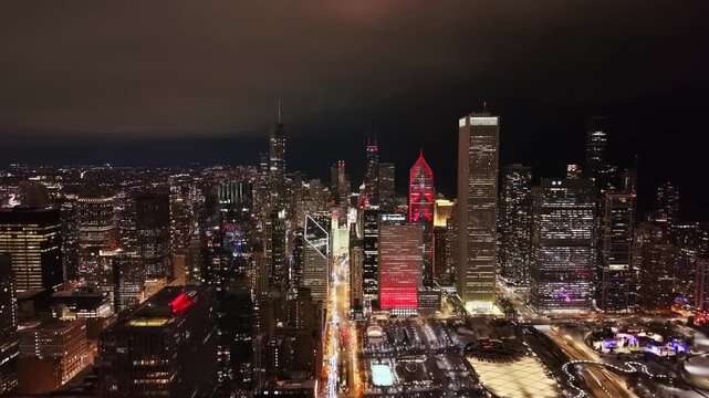 Breathtaking night aerial perspective of the Chicago skyline, showcasing the illuminated Two Prudential Plaza in red, Aon Center, and Millennium Park.