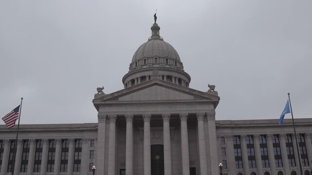 Oklahoma state capitol building exterior view with american and state flags waving on cloudy day