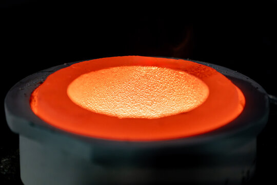Close up of molten metal being poured into a heated crucible during casting showing intense heat, flame, and thermal energy.