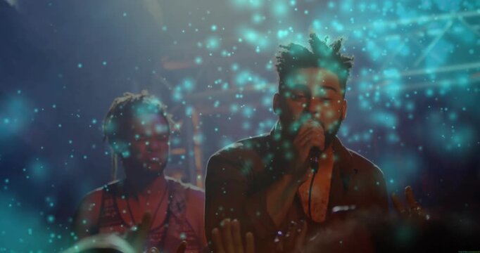 Singer grabbing mic, starting music to engage crowd, singing, gesturing with teal particles onstage