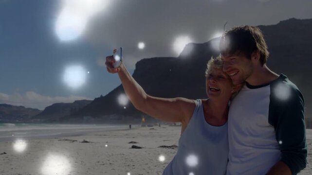Woman extending phone, man wrapping arm for selfie as bokeh drifting obscuring faces for travel