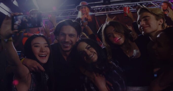 Friends raising smartphone capturing selfie at music concert, checking selfie amid animated flares