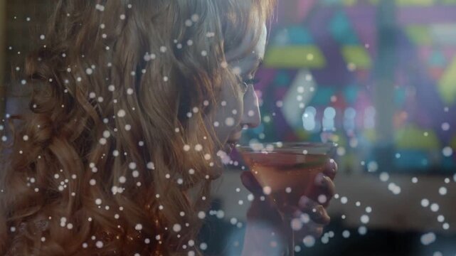 Female patron lifting martini glass at bar, sipping and tasting while droplets drifting across lens