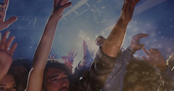 Group of concertgoers raising hands toward stage light after music drop, with confetti floating