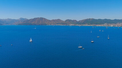 Obraz premium Marmaris, Turkey. Low aerial panoramic view of Marmaris Bay filled with yachts. The city and shoreline are visible in the distance on a bright summer day.. Aerial View