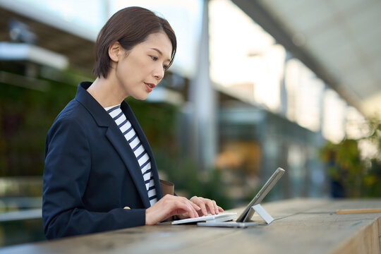 Japanese businesswoman working on tablet outdoors in urban green space