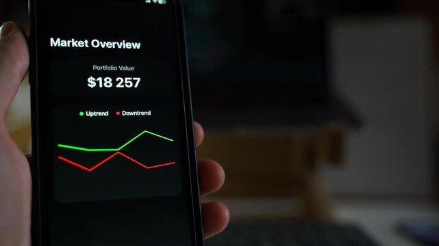 Hand holding smartphone with open market overview app displaying portfolio value in live mode