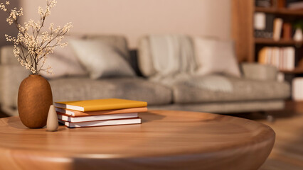 Books and flower vase on round wooden table with grey sofa aside shelf and white wall in living room © bongkarn