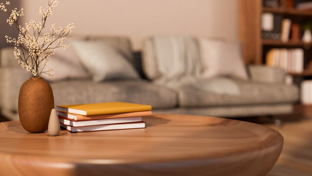 Books and flower vase on round wooden table with grey sofa aside shelf and white wall in living room