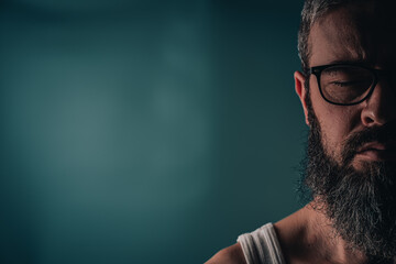 Man with glasses and beard stands against a light background and closes eyes © mykhailo