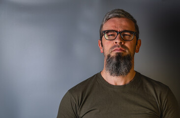 Obraz premium Man with a beard and glasses stands in front of a gray background