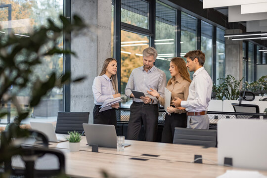Group of business people standing together and discussing their work and projects, having a team meeting in an office.