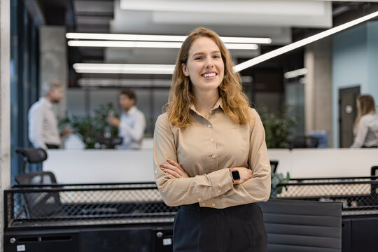 Attractive young businesswoman standing on the table, looking at camera with colleagues on the background