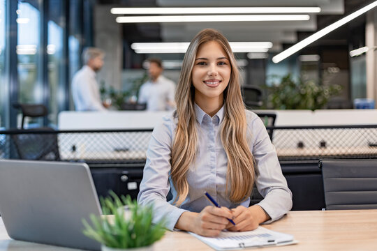 Young business woman is using laptop while sitting in the office, smiling