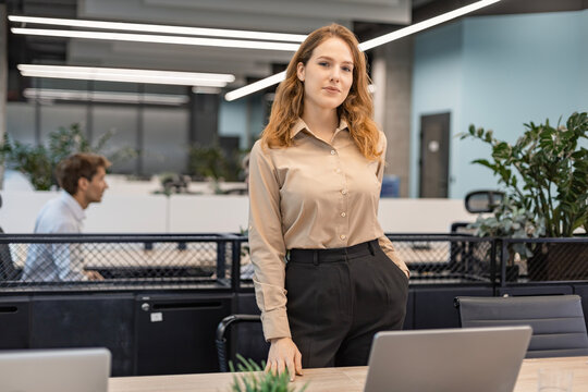 Attractive young businesswoman standing on the table, looking at camera with colleagues on the background