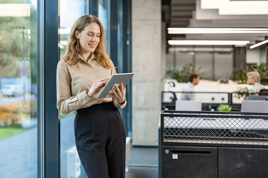 Young elegant business woman standing with digital tablet near office window