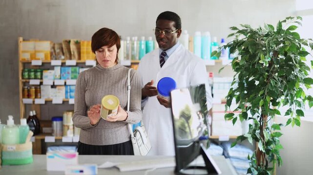 Adult woman buyer choosing baby formula with help of adult man pharmacist in pharmacy
